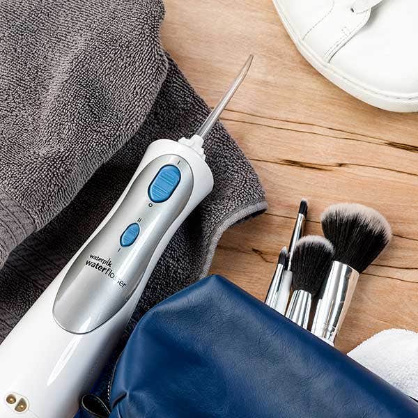 Cordless water flosser on a towel next to makeup brushes